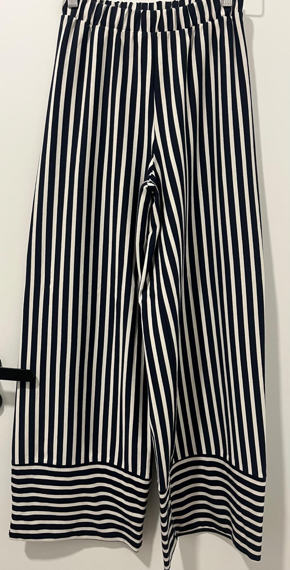 Black and white vertical striped trousers hanging on a hanger. The hem has horizontal stripes.