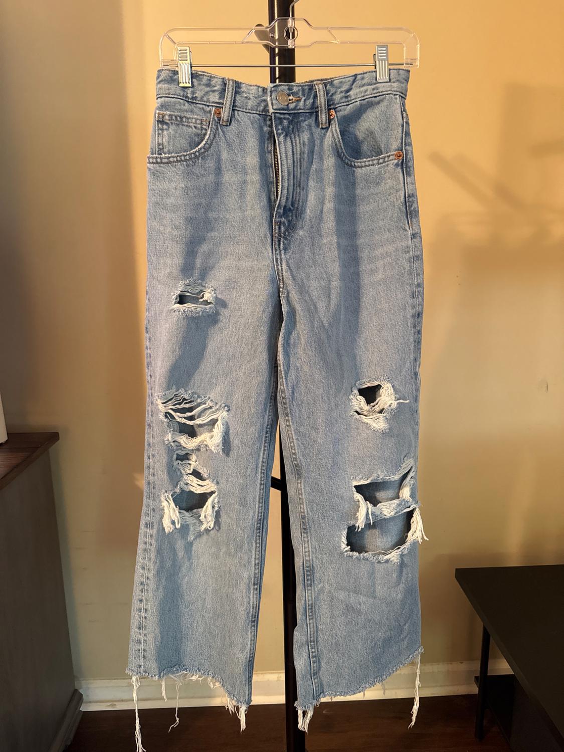Front view of blue jeans with rips and visible front pockets.