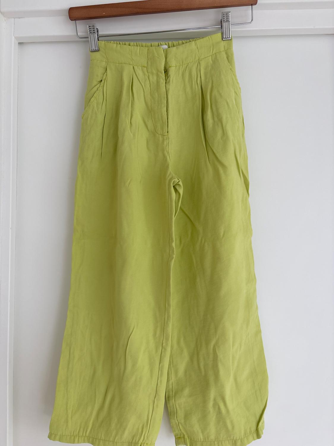 Lime green wide-leg trousers hanging on a wooden hanger against a white background.