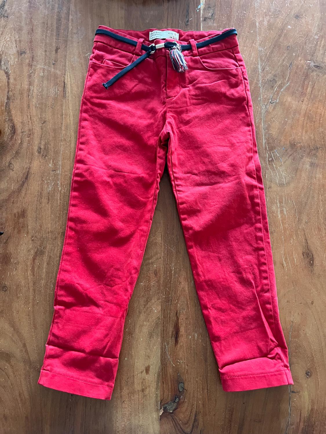 Red boys' trousers with a blue belt and tassel, on a wooden surface. Label visible on the inside of the waistband.