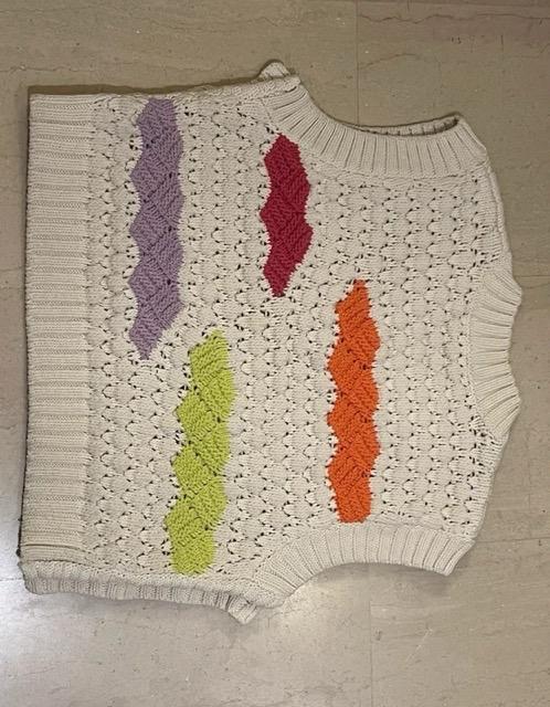 White knitted waistcoat with zigzag patterns in purple, red, green and orange on a light wooden background.