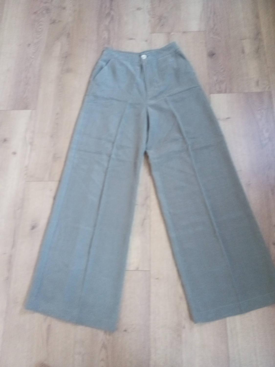 Khaki wide-leg trousers on a light wooden floor. Simple design with side pockets and button fastening.