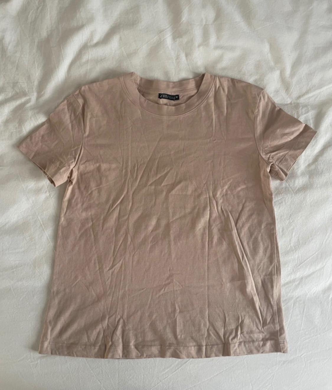 Short-sleeved T-shirt in a light pink shade, laid out on a crumpled white fabric surface.