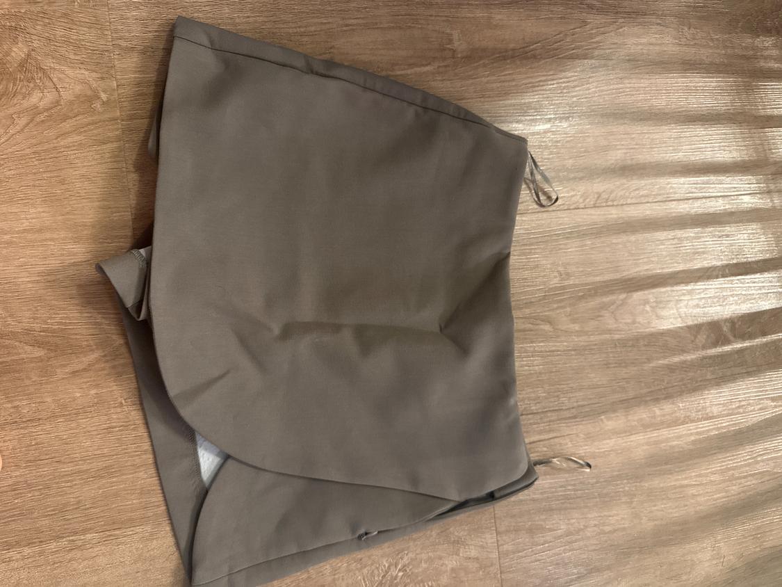 Grey shorts folded on a wooden floor. Plain fabric with a wrap-around design and ties at the sides.