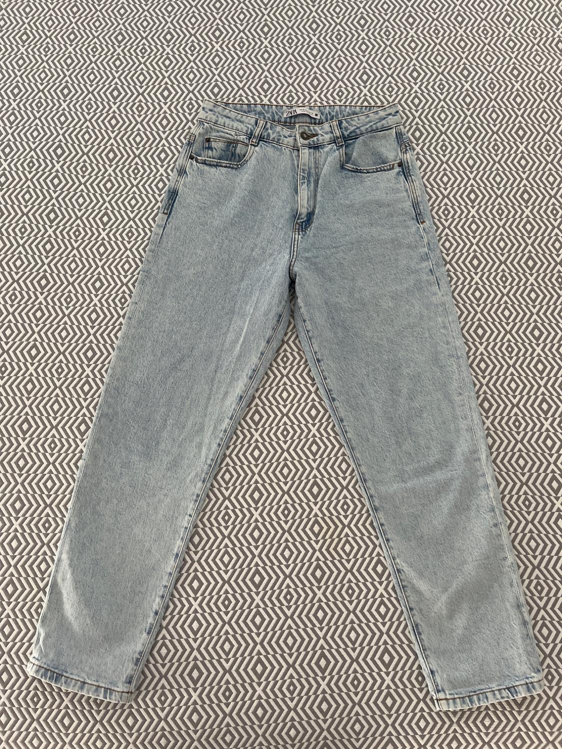 Light blue jeans on a geometric background in shades of grey and white. Visible label at the waist.