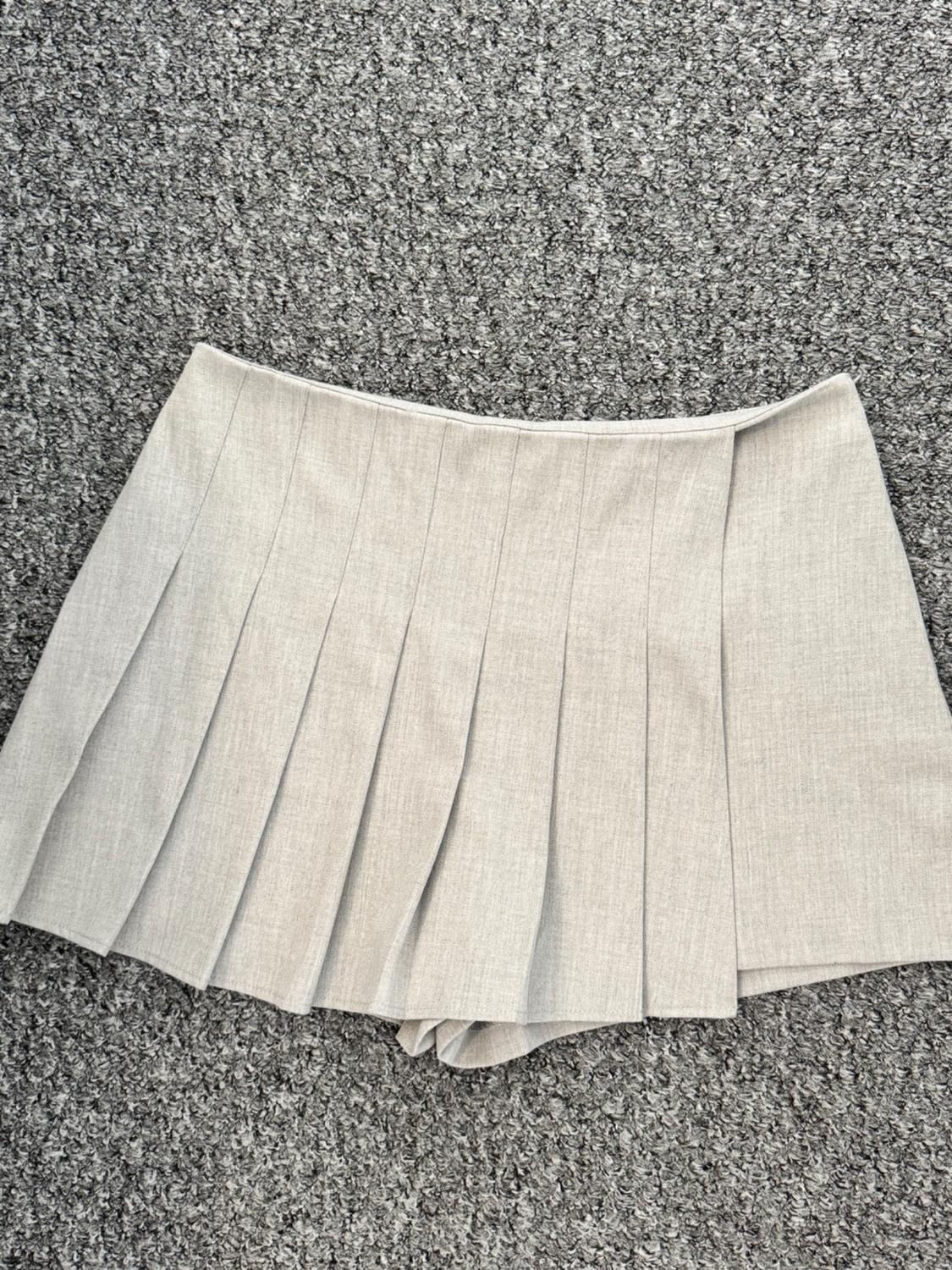 Short, light grey skirt with visible pleats, placed on a rough textured grey carpet.