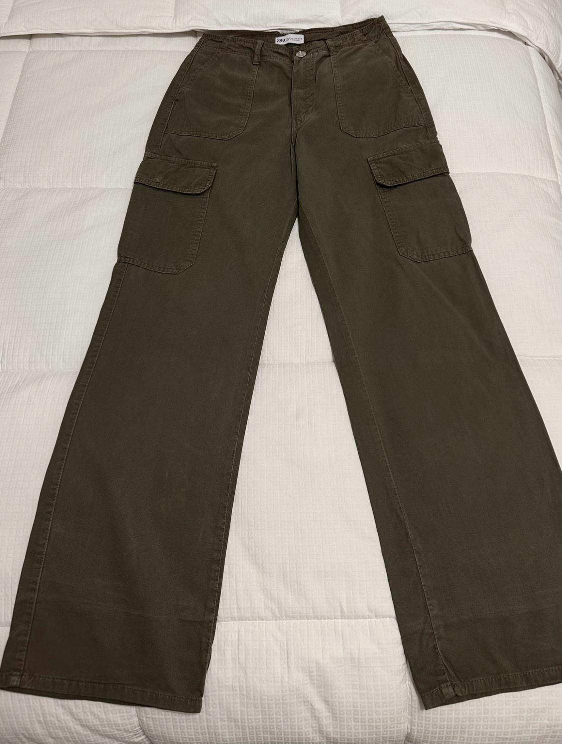 Olive-green wide-leg cargo pants with front and side pockets, laid out on a white comforter.