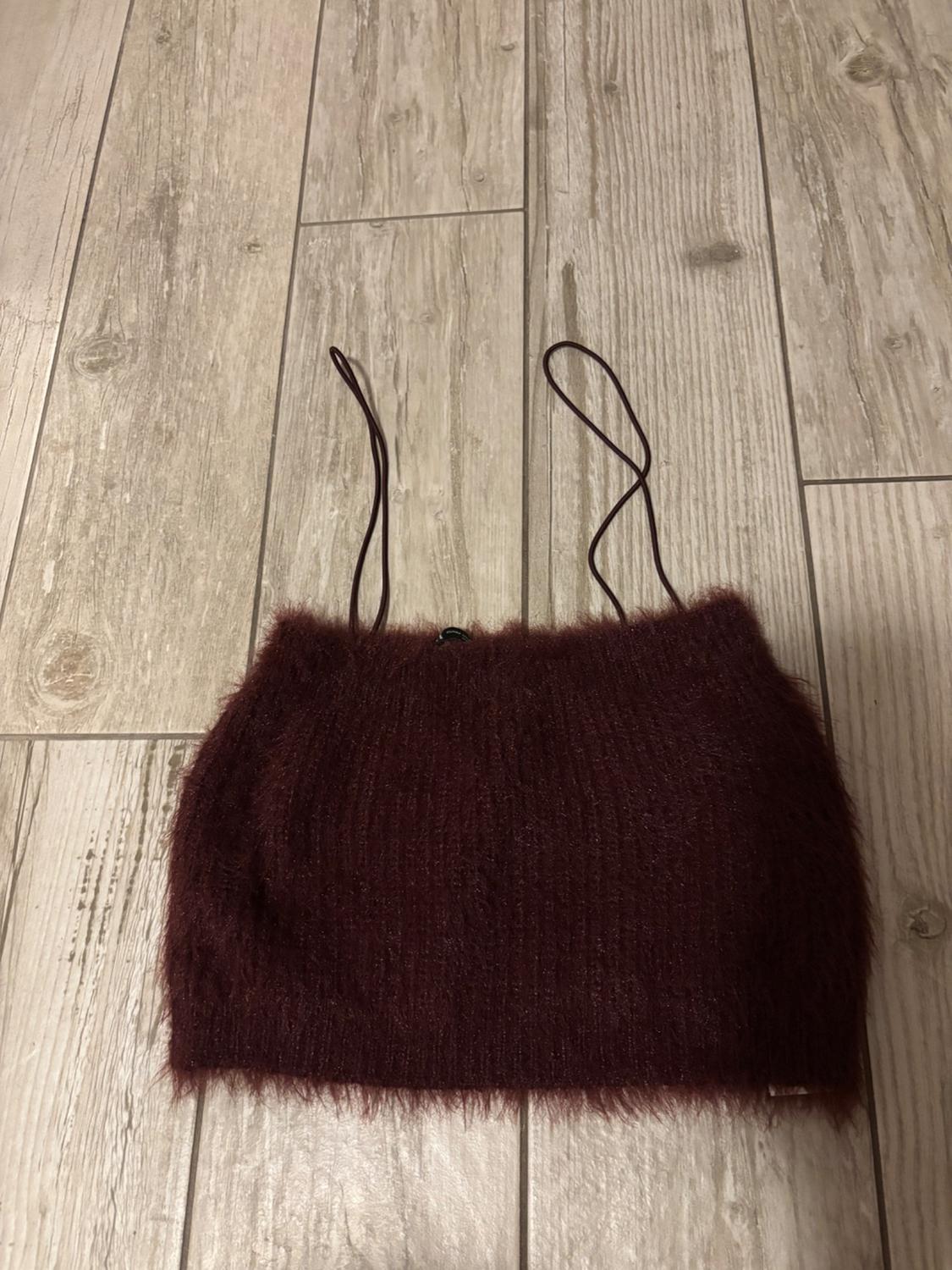Burgundy cropped top with thin straps and a furry texture, laid on a light wooden floor.