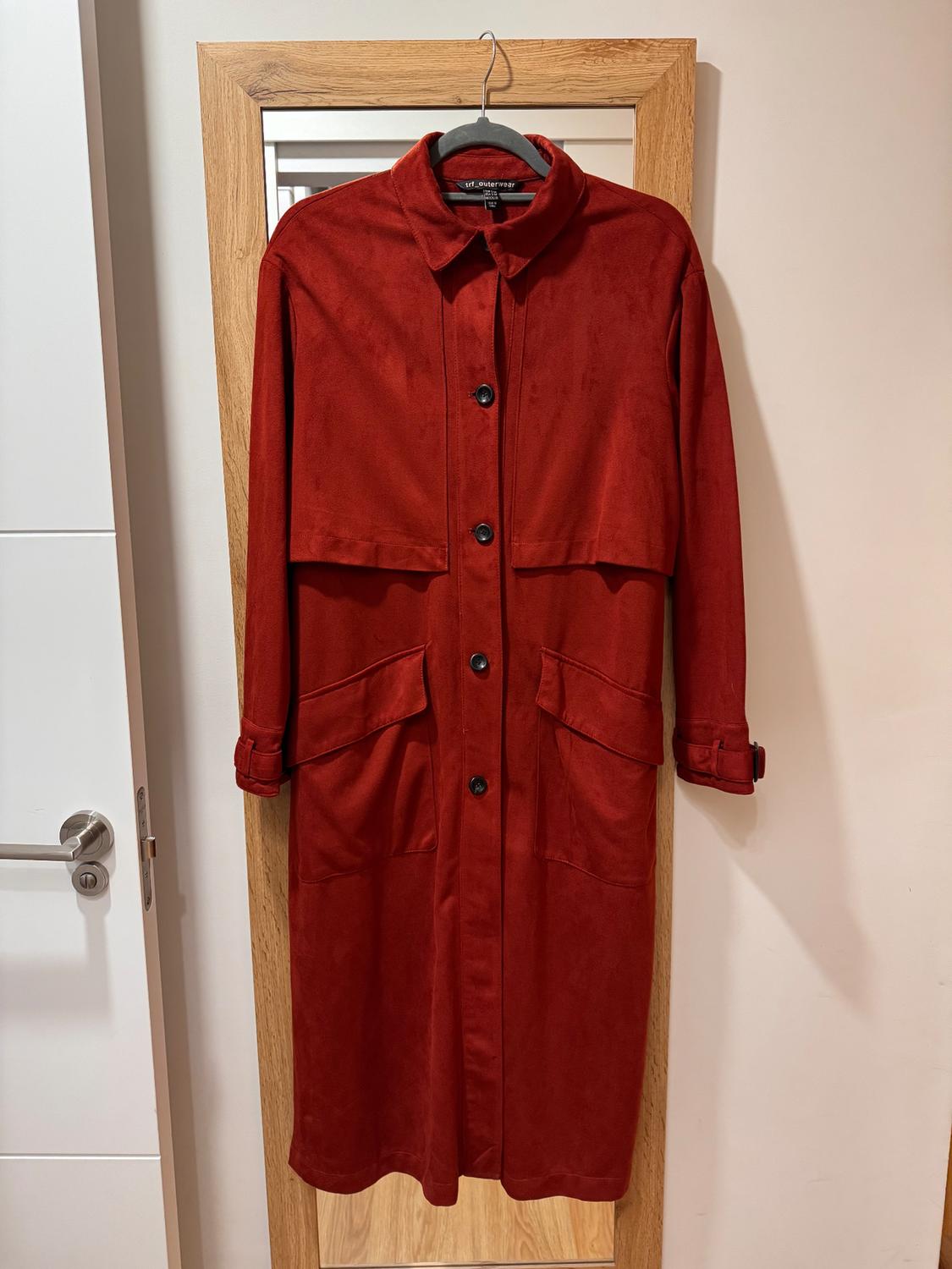 Red coat hanging on a hanger in front of a wooden-framed mirror. It has black buttons and large pockets.