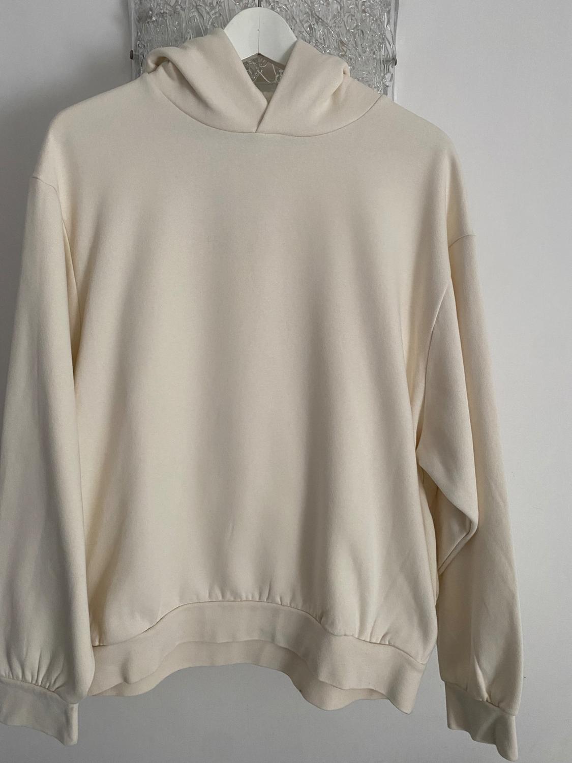 Beige hoodie hanging on a white hanger against a light grey background. Simple, relaxed design.