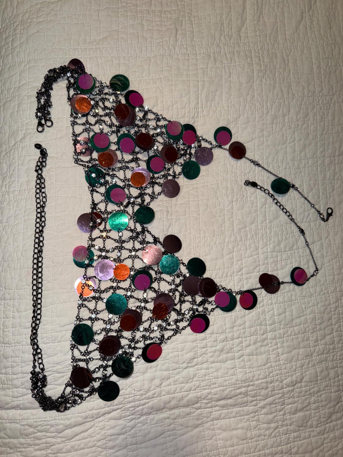 Halter top with dark chains, rhinestones and large round sequins in vibrant metallic tones, on light-coloured quilted fabric.