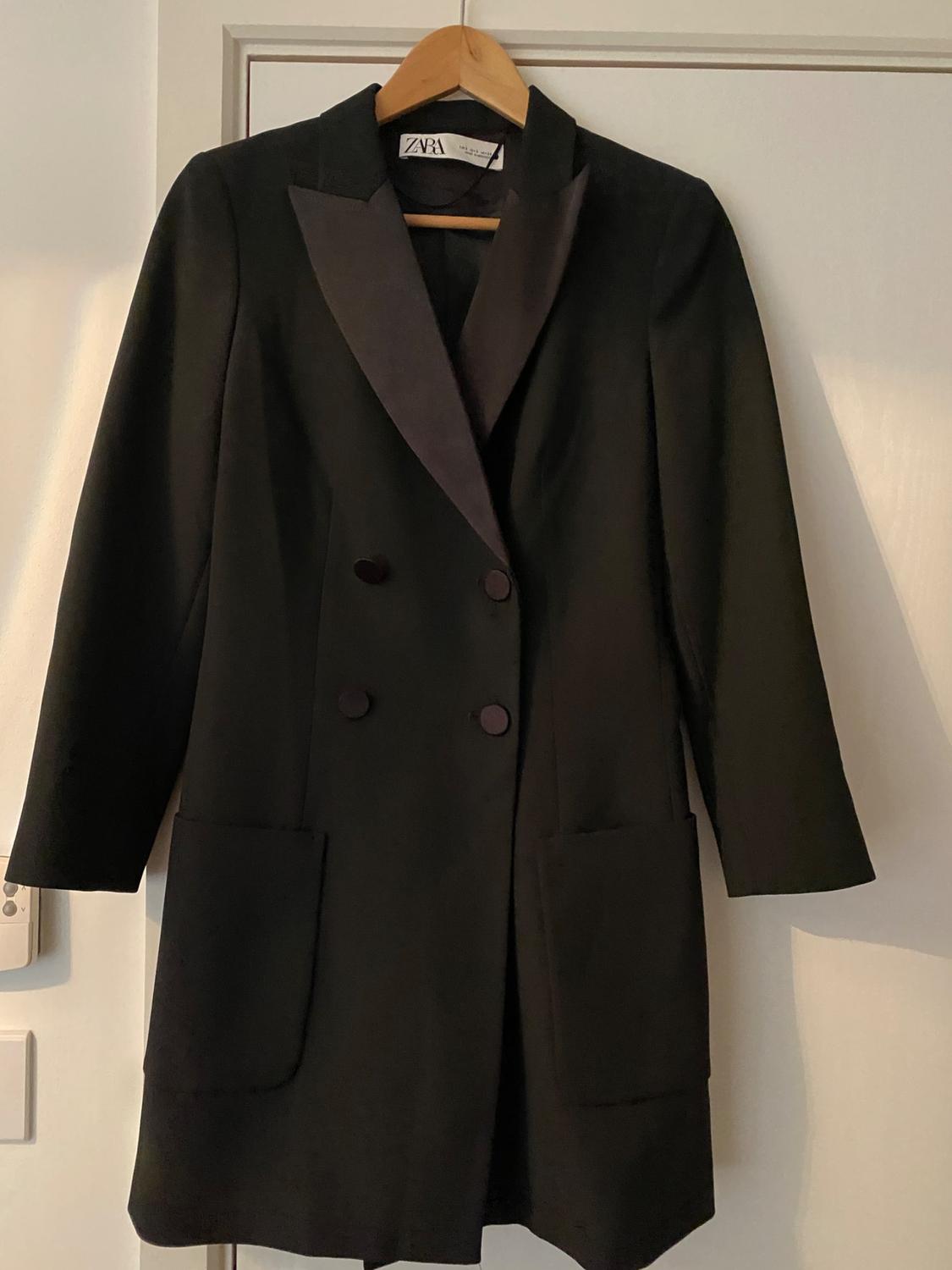 Front view of a black coat with wide lapels and double-breasted buttons, large side pockets.