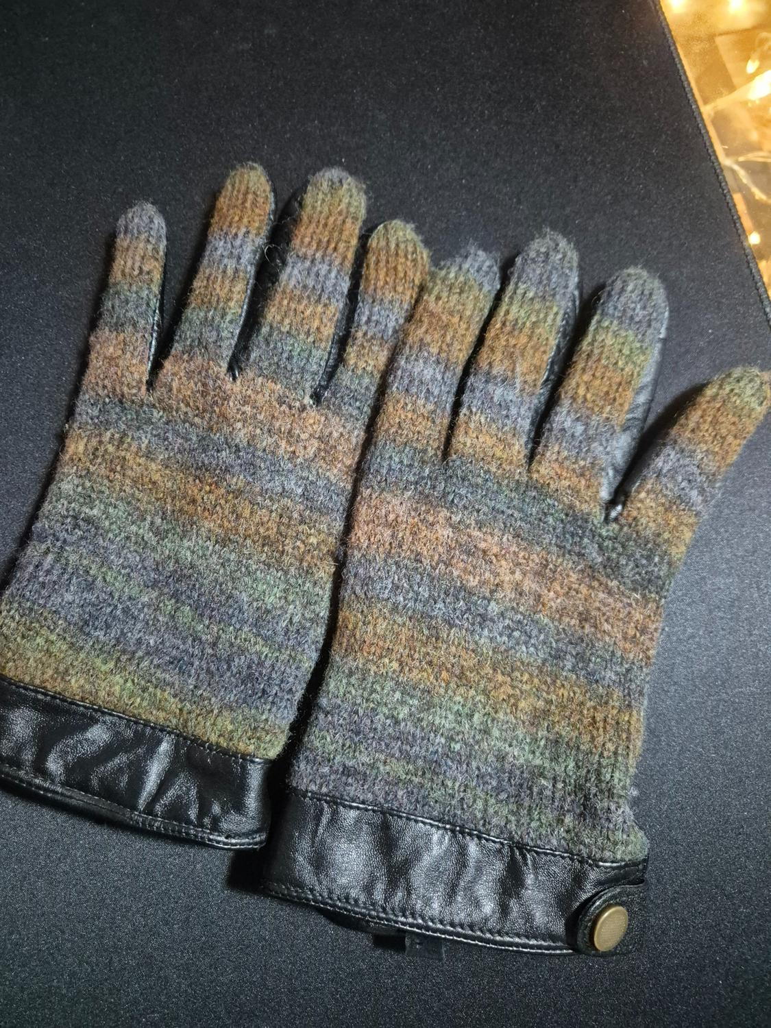 Multicoloured striped wool gloves with black leather cuffs and button, on an illuminated black background.