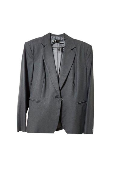 Black suit jacket hanging, with classic lapels and one button. Visible label inside with the brand name.
