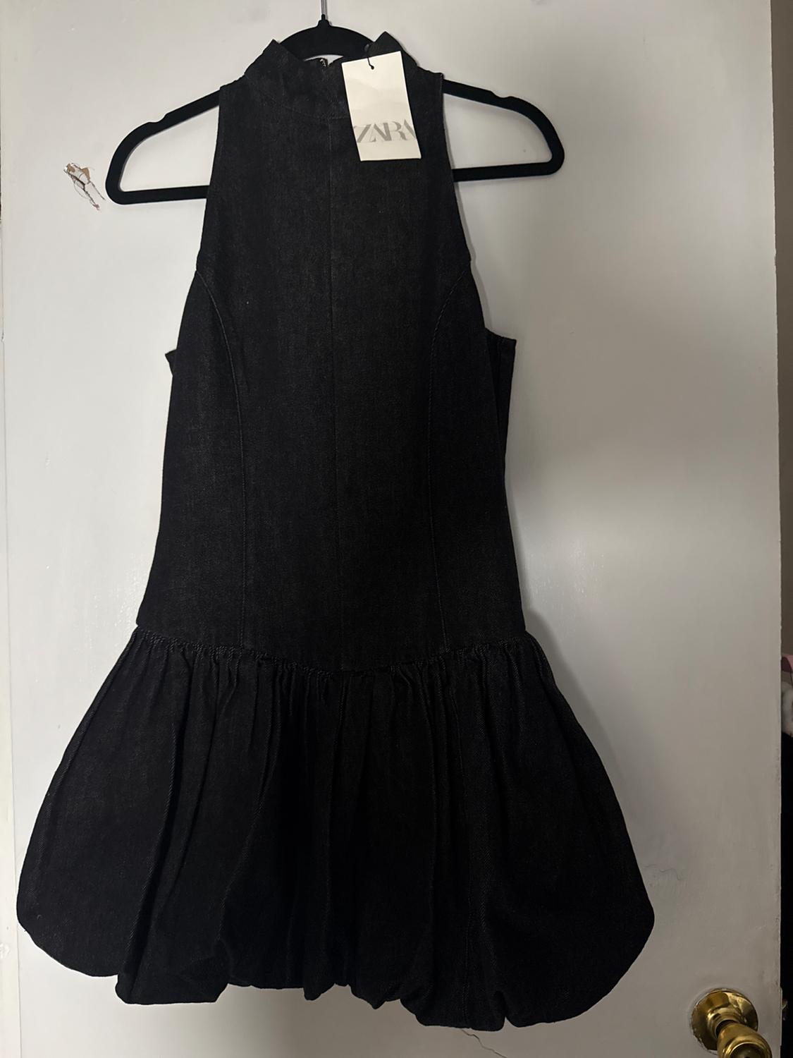 Sleeveless black dress with voluminous skirt, hanging on a black hanger. Visible tag with text "ZARA". White background.