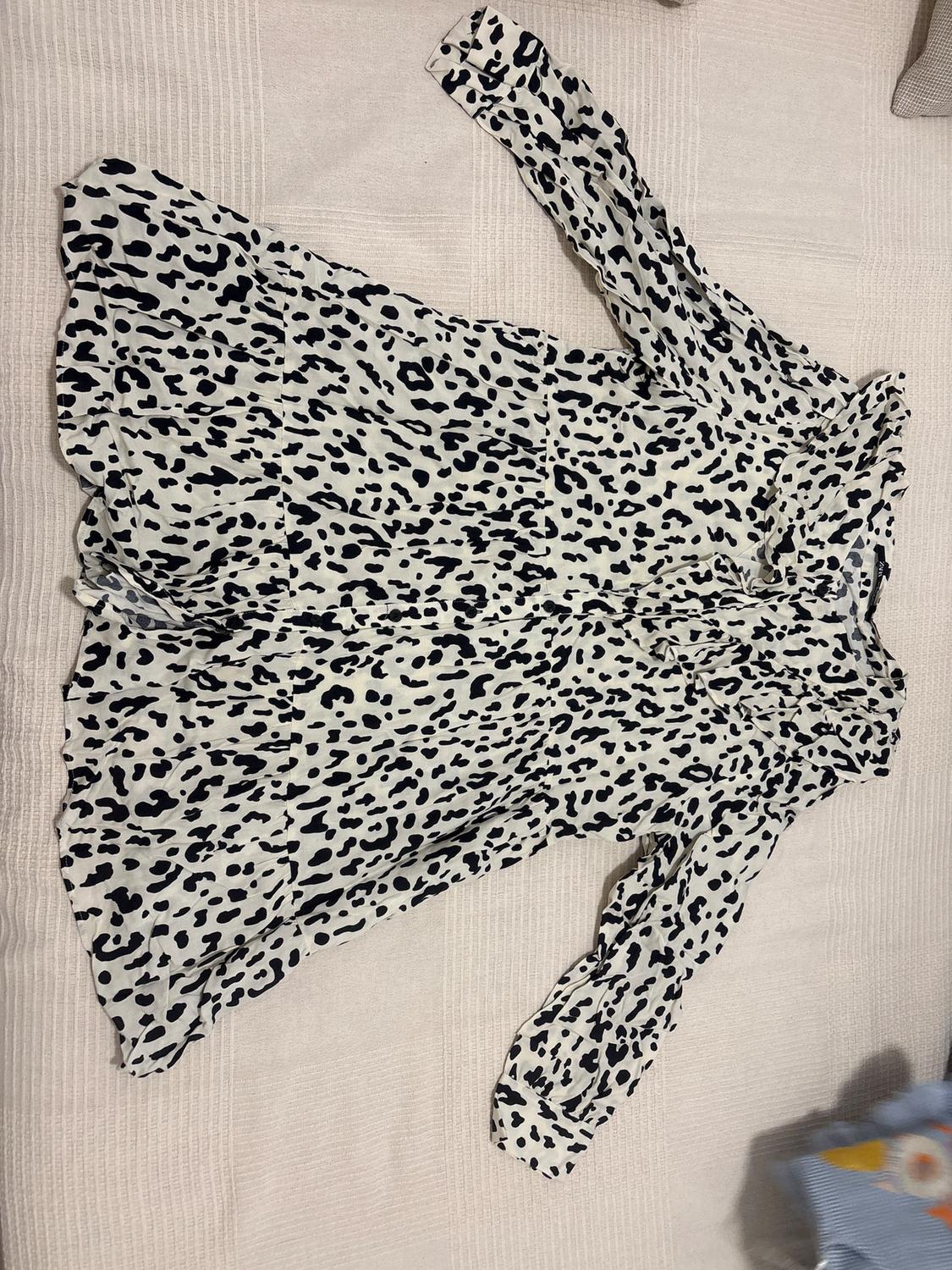 White dress with black spot print, long-sleeved, spread out on a light textured surface.