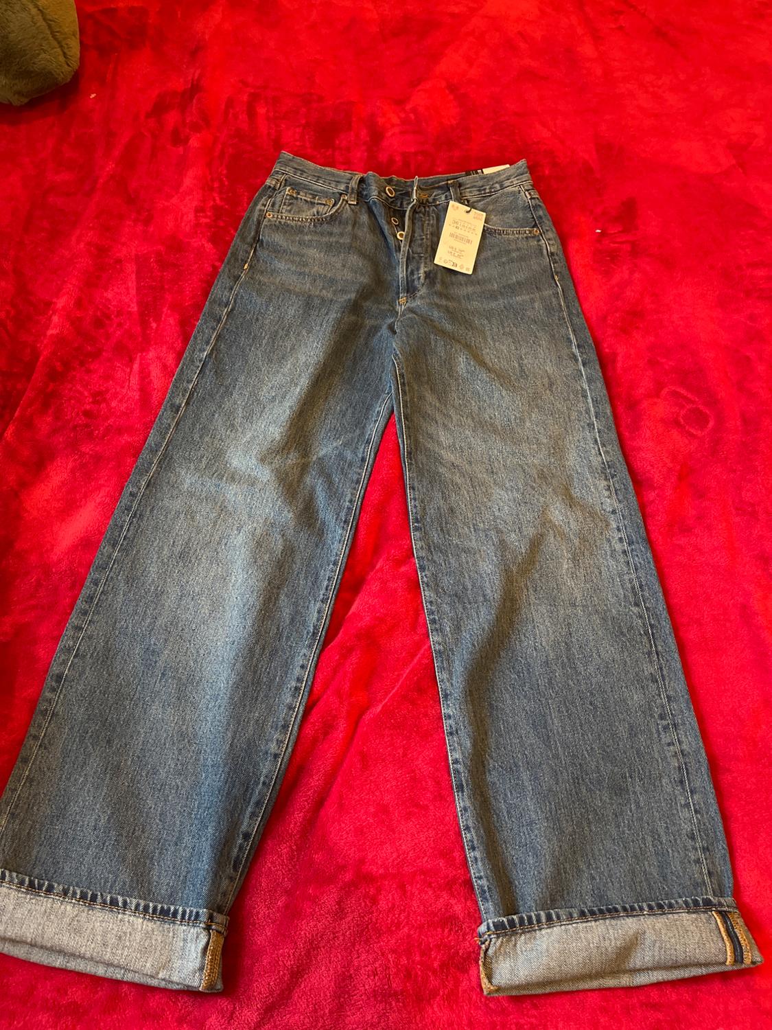 Wide-leg jeans with hem, swing tag, on a vibrant red background.