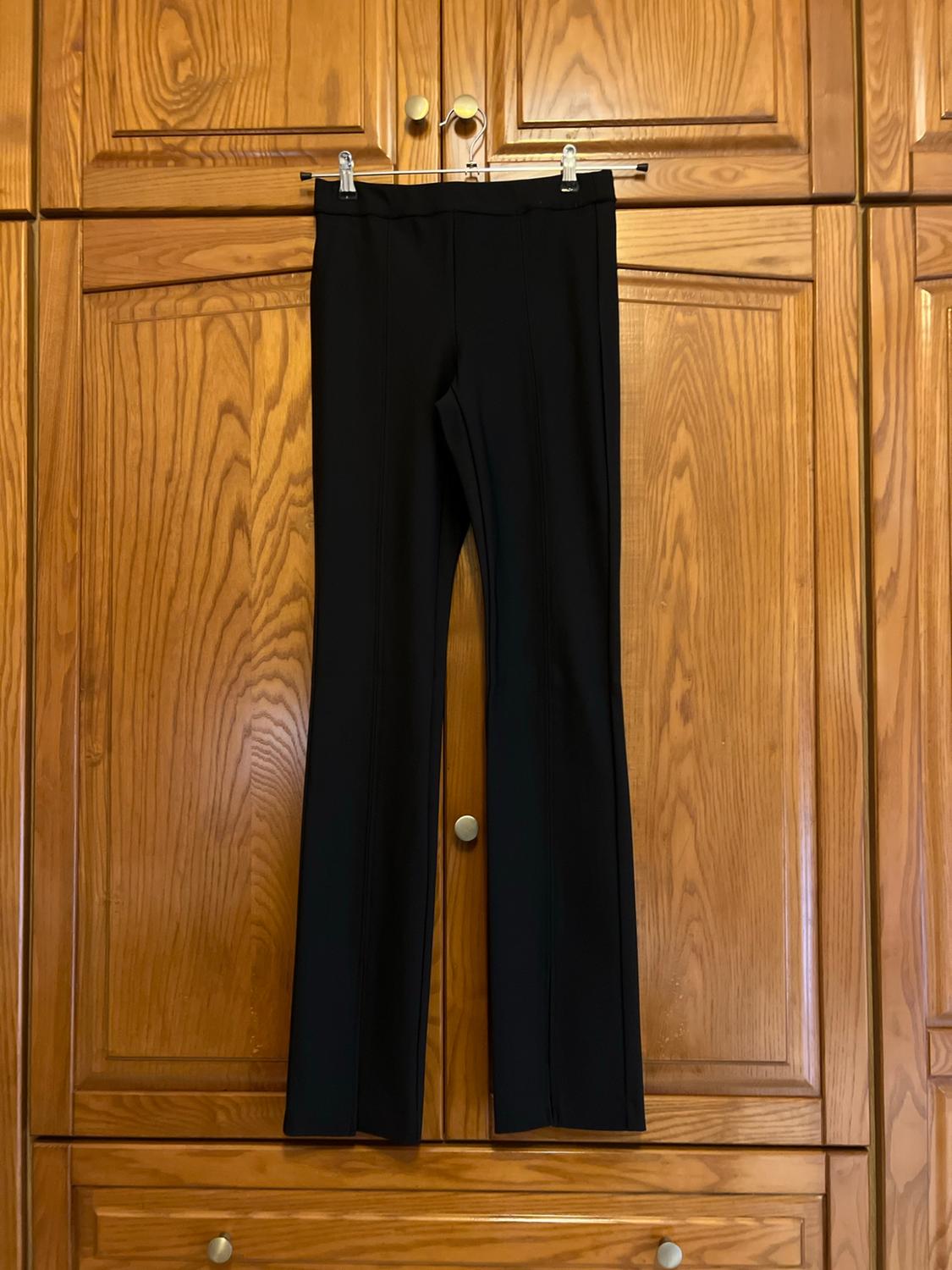 Black trousers with front seams hanging from a hanger in a classic wooden wardrobe, conveying a casual and relaxed style.