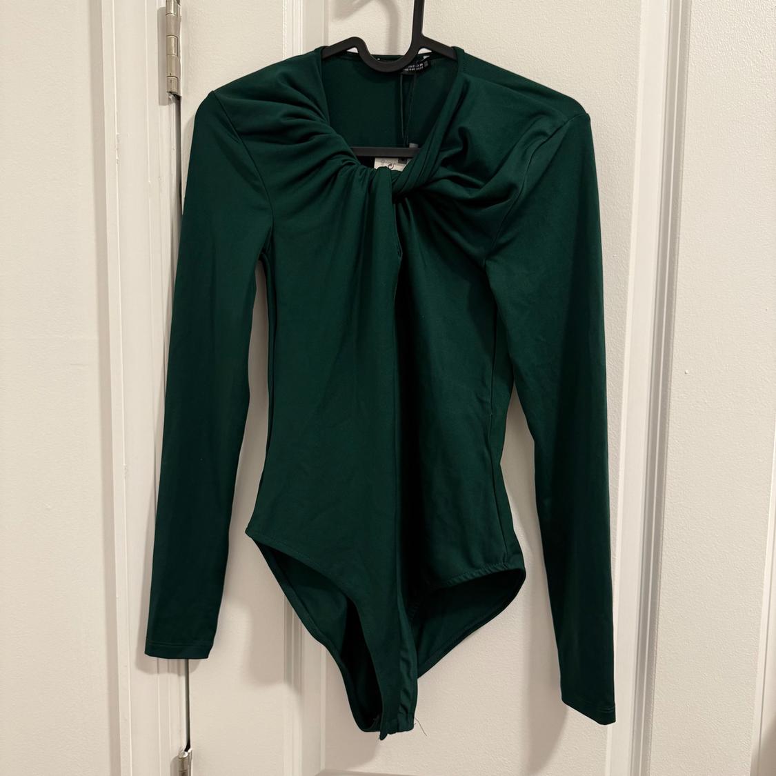 Dark green long-sleeved bodysuit with knot detail on the neckline, hanging on a hanger over a white door.