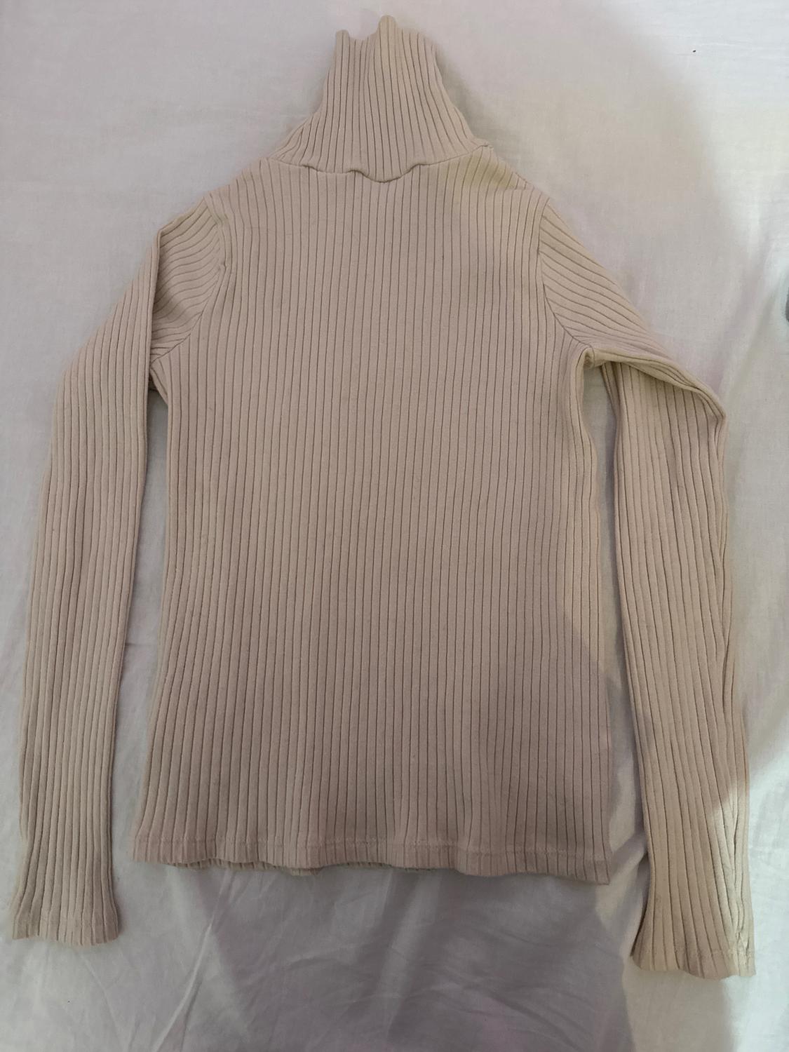 Ribbed knit beige sweater with a high neck and long sleeves, spread out on a white surface.