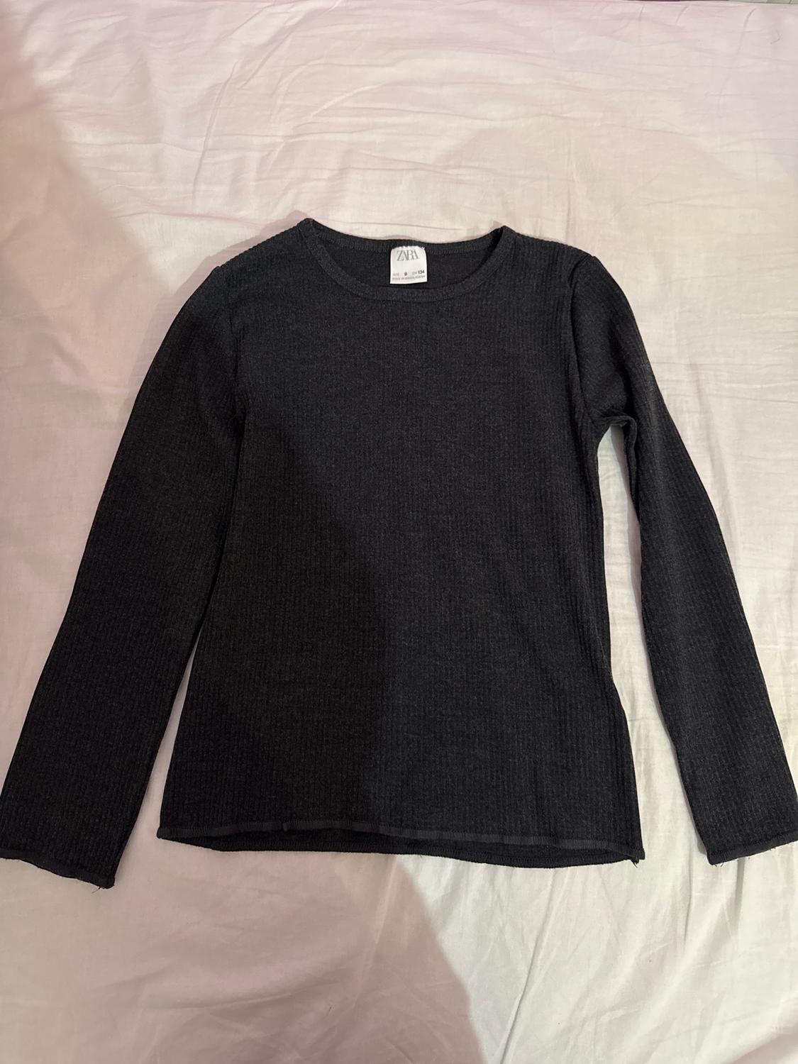 Black long-sleeved sweater on a white surface. Visible tag on the collar with text "ZARA".