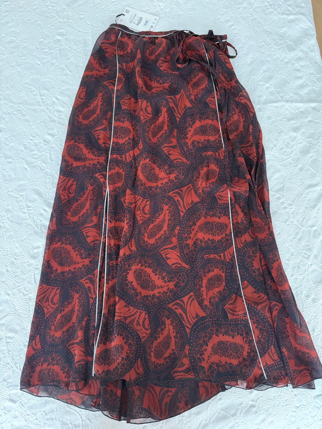 Long wrap skirt with a red pattern on a dark background and white trim, spread out on a textured white fabric surface.