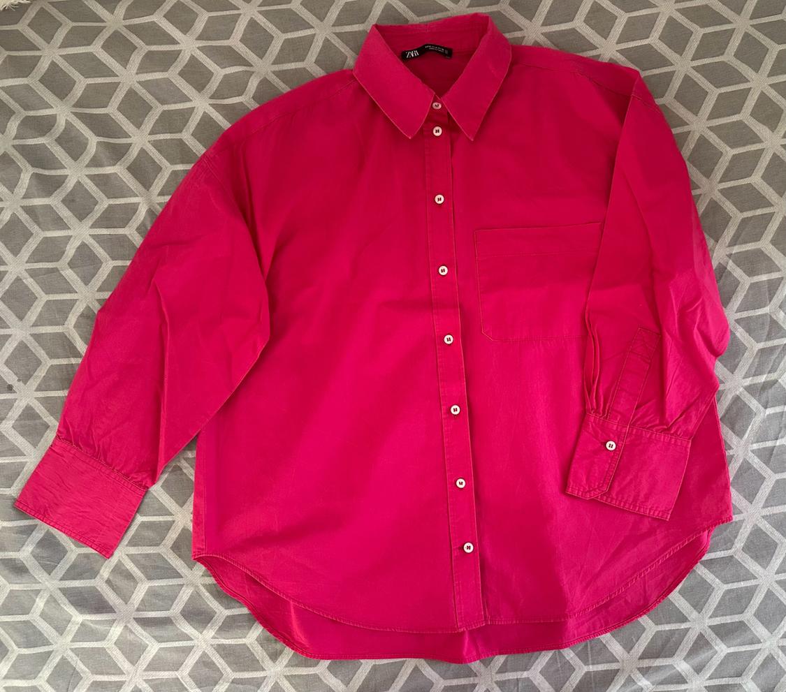 Fuchsia pink long-sleeved button-up shirt with a pocket, set against a grey and white geometric background. Label with ZARA text on the collar.