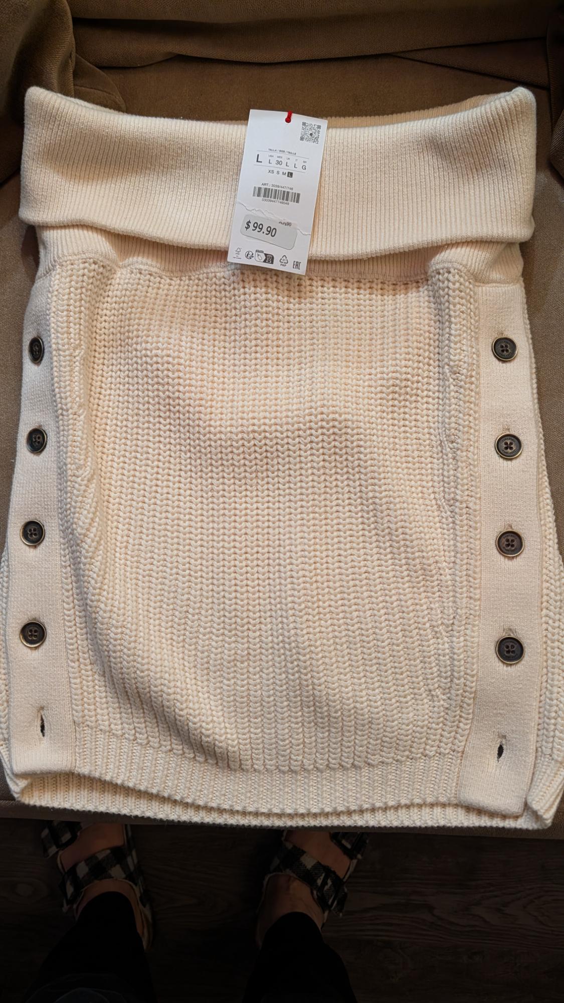 Beige knitted skirt with side buttons and a price tag of $99.90 on a brown background.