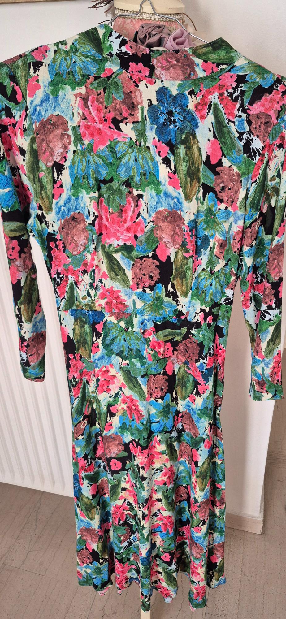Long-sleeved dress with a floral print in shades of pink, blue, and green on a black background, hanging on a mannequin.