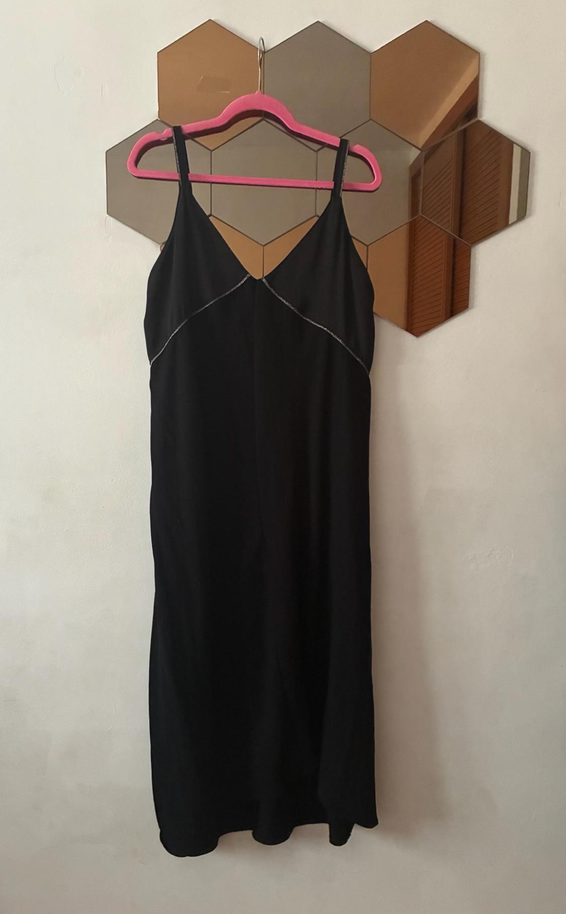 Black strappy dress with silver detailing on the neckline, hanging on a pink coat hanger over a hexagonal mirror on a white wall.