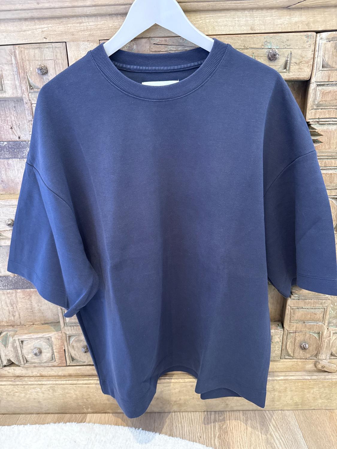 Blue short-sleeved t-shirt hanging on a white hanger, against a wooden background with carved drawers.