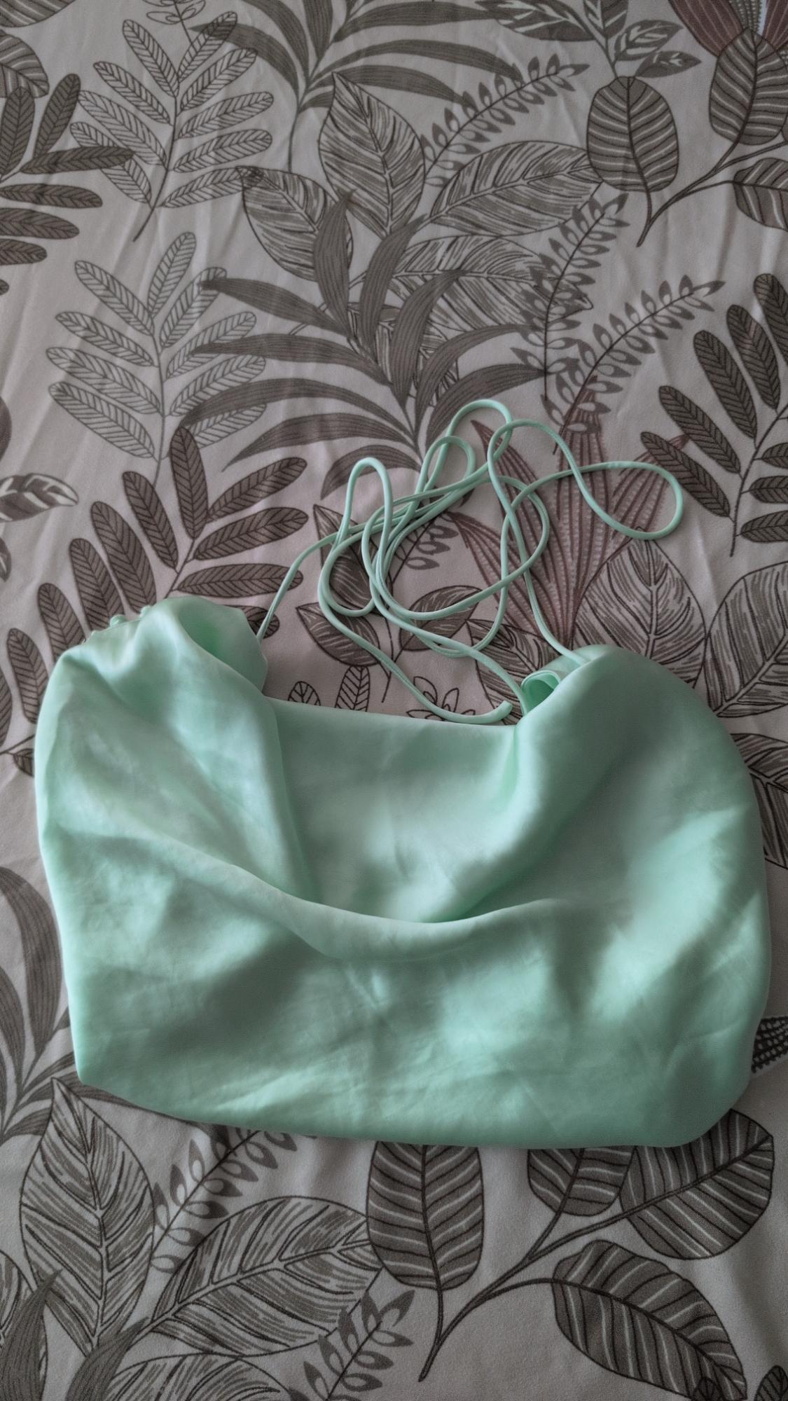 Light green satin camisole with thin straps, set against a leaf-print background.
