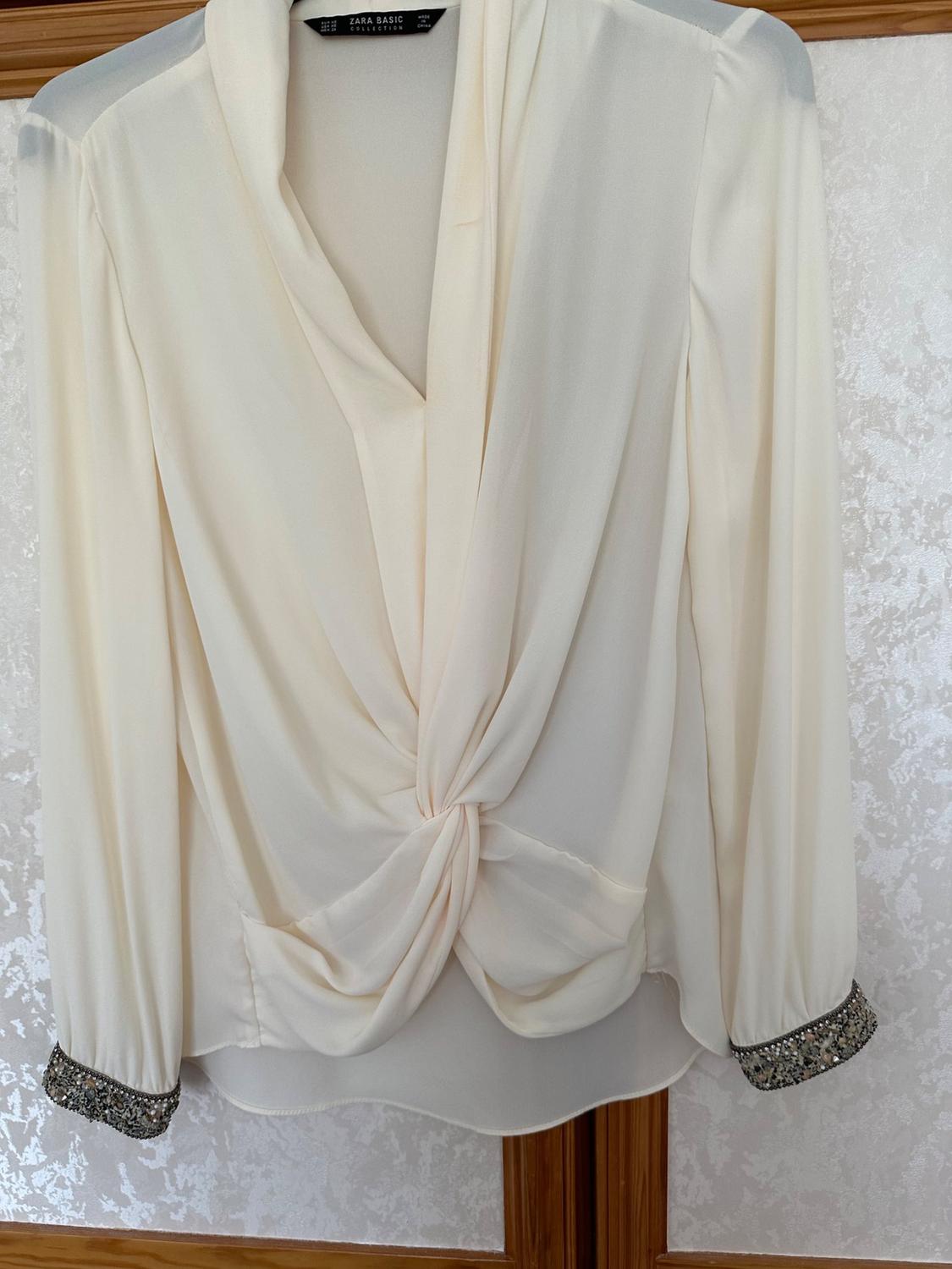 Front view of white blouse with draped detail on the front and embellished cuffs.