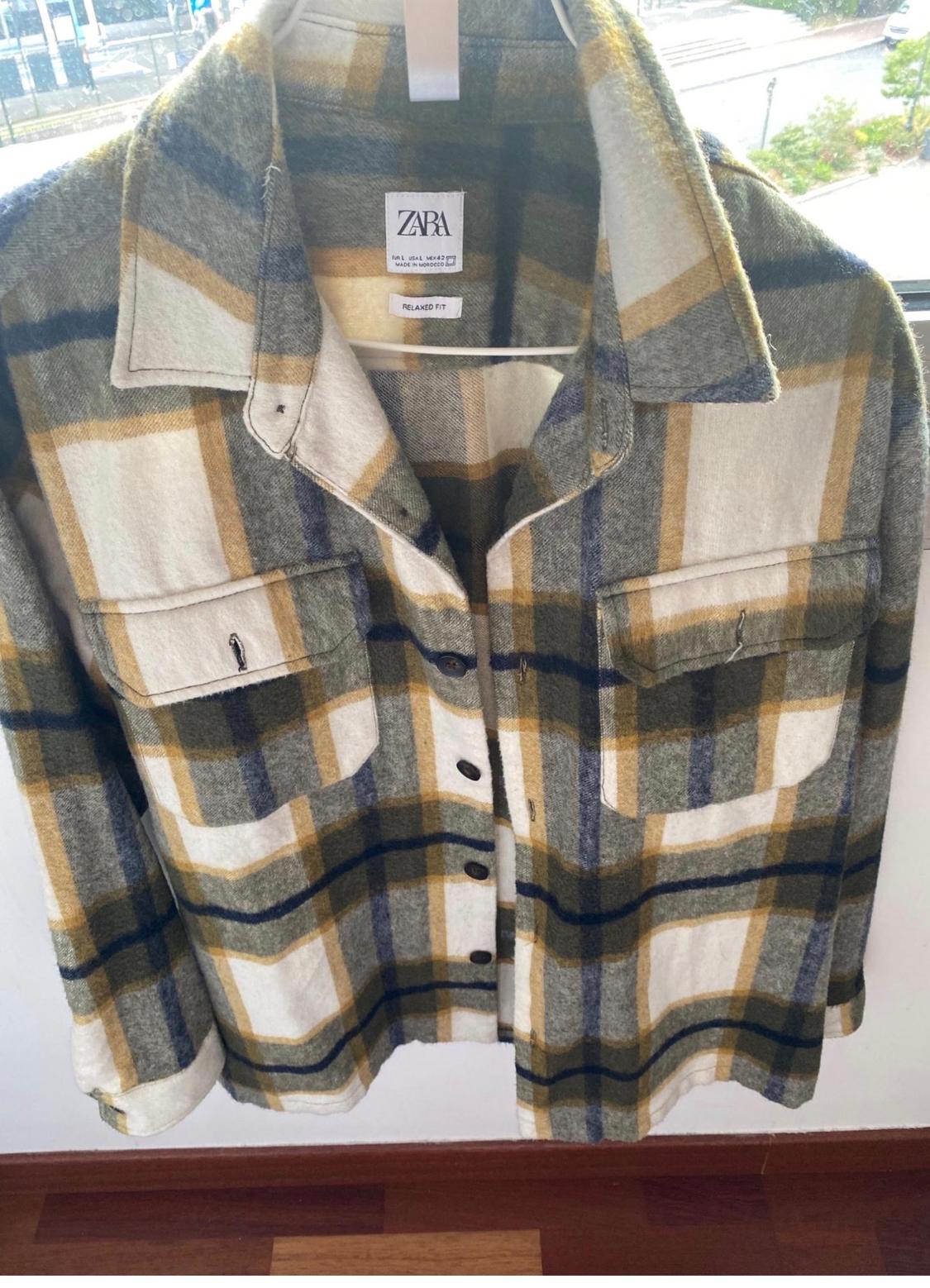 Checked shirt in shades of green, blue, and beige hanging on a hanger. Visible label: "ZARA", "RELAXED FIT".