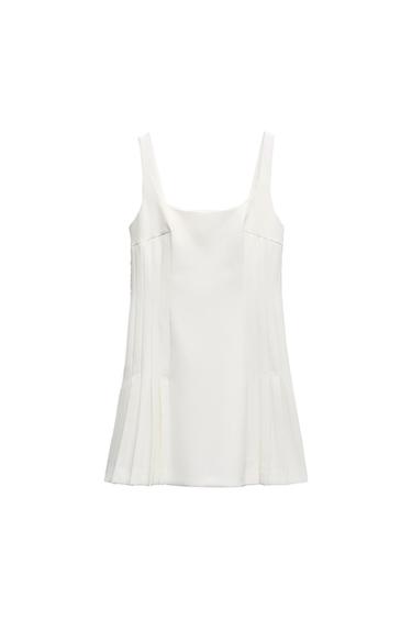 Front view of a white blouse with straps and decorative pleats on the sides.