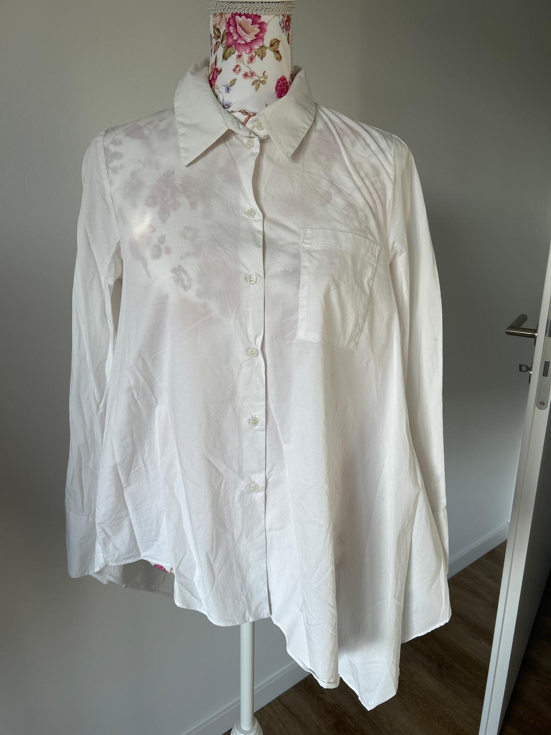 White long-sleeved shirt on a mannequin with a floral print. Minimalist interior background with a white door and wooden floor.