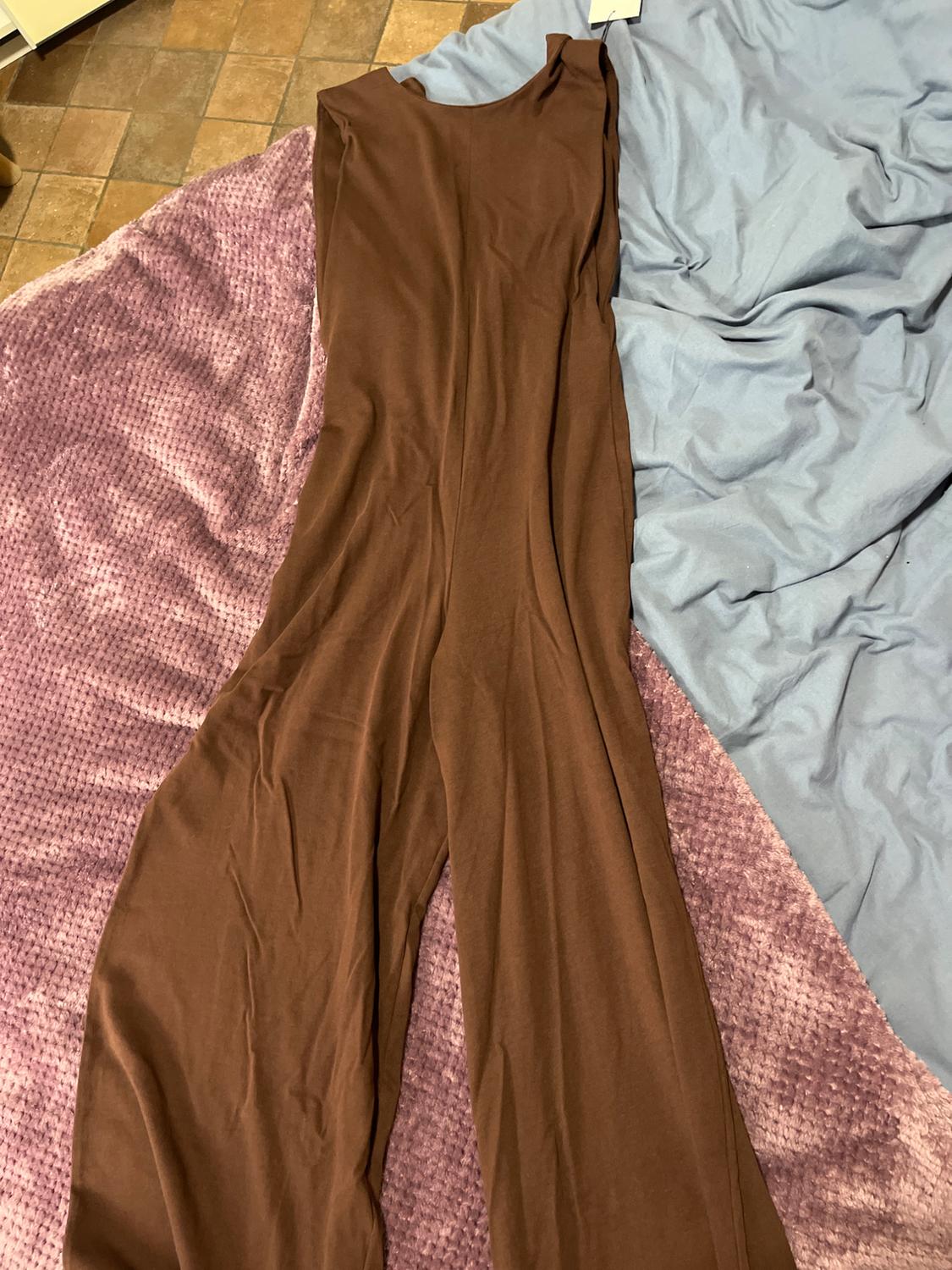 Brown sleeveless jumpsuit laid out on a purple and blue blanket on a brown tiled floor.