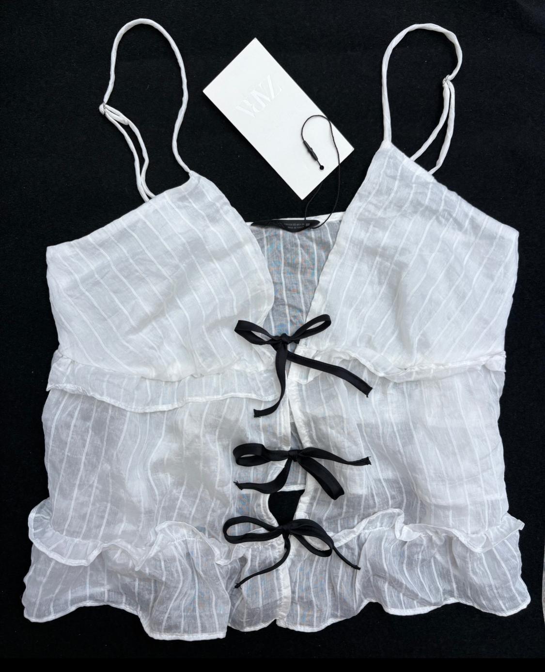 White ribbed camisole top with frills and black ribbon details on the front. ZARA label on a black background.