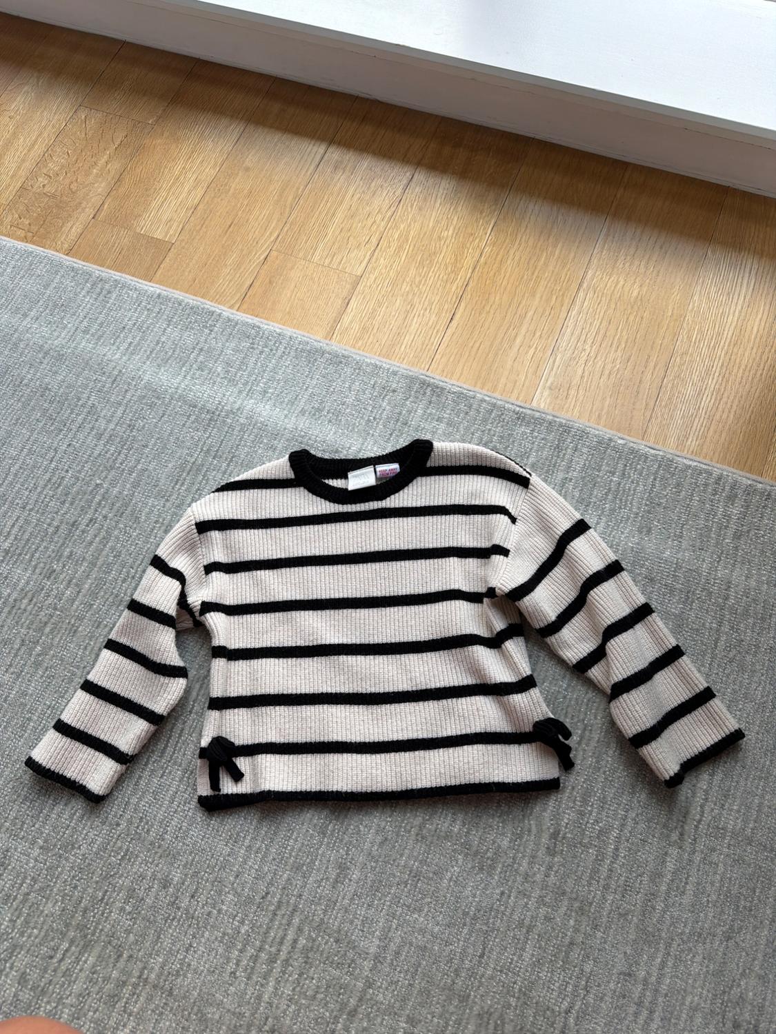 Black and white striped jumper on a grey rug and light wood floor.