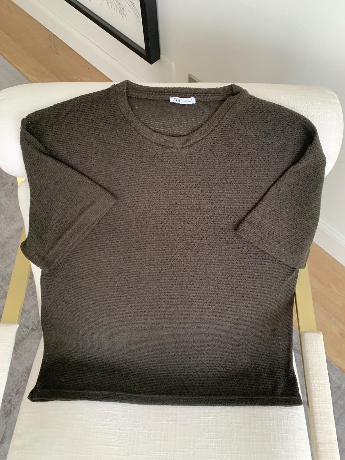 Dark green short-sleeved knitted T-shirt on a white chair. ZARA label visible at the neck.