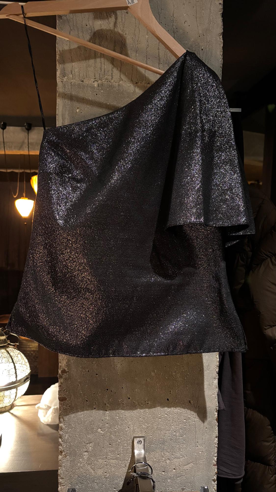 Shiny black fabric draped on a wooden hanger against a concrete wall, with warm lights in the background.