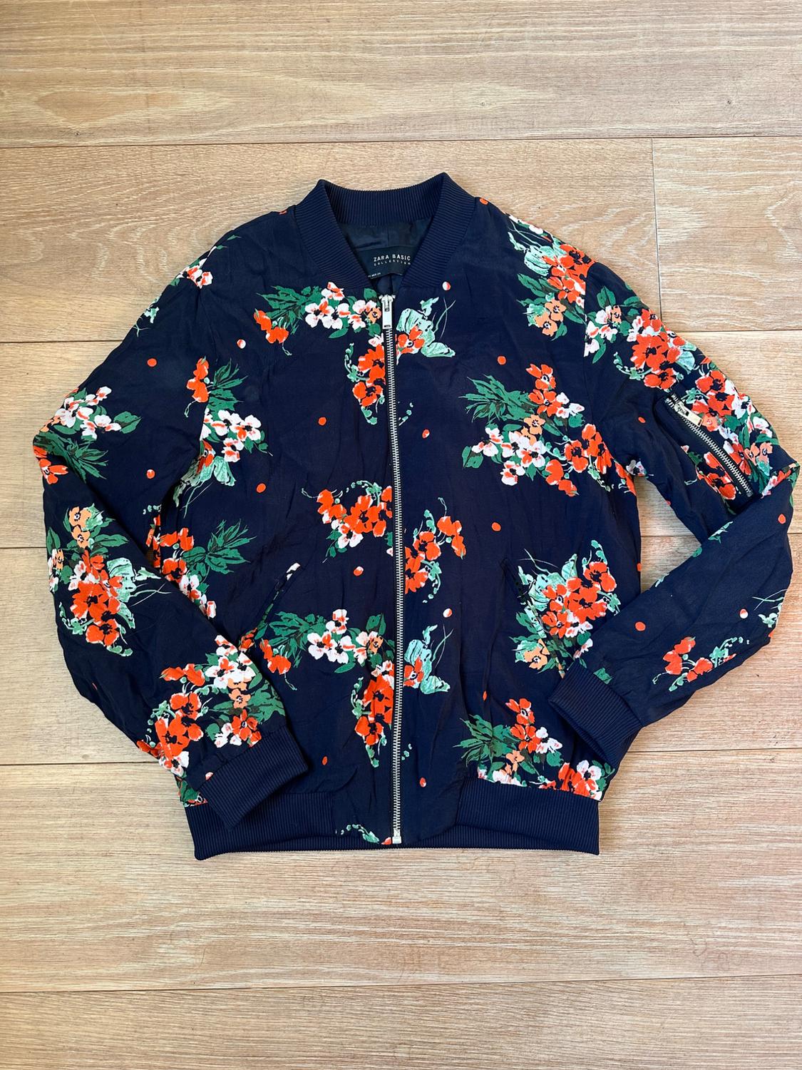 Front view of a blue jacket with a red and green floral print, zip fastening and a round neck.