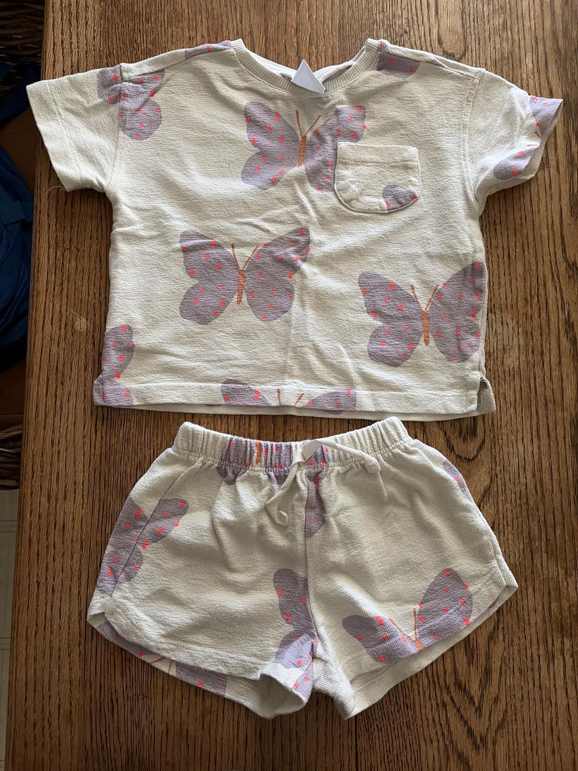 Children's beige T-shirt and shorts set with grey and pink butterfly print on a wooden table.