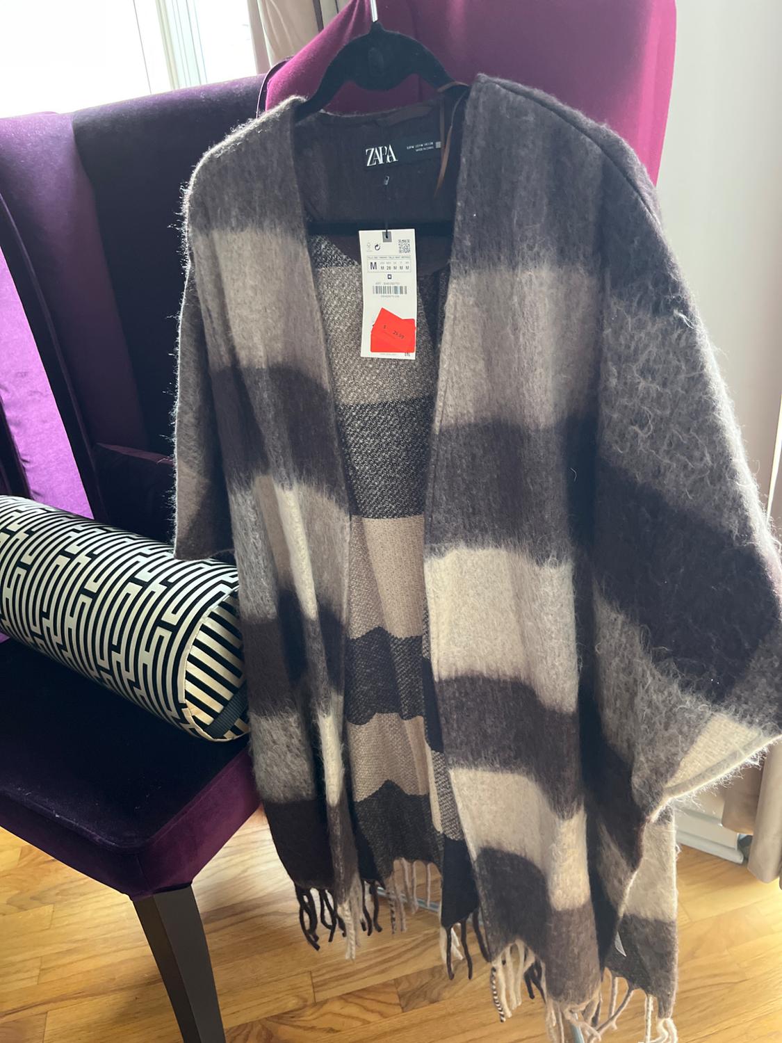 Grey and black striped cardigan hanging on a hanger over a purple chair. Price tag visible. Wooden floor.