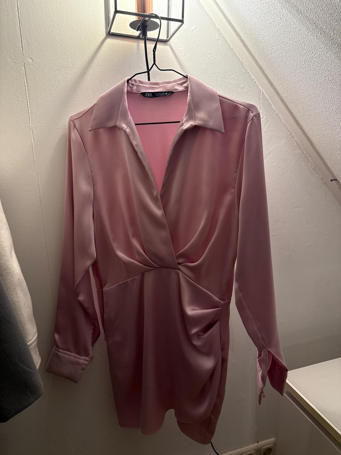 Pink satin dress with a classic collar and long sleeves, hanging on a black hanger in a well-lit room.