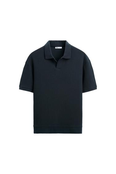 Black, short-sleeved polo shirt with a ribbed texture and classic collar. Visible label on the inside of the neck. White background.