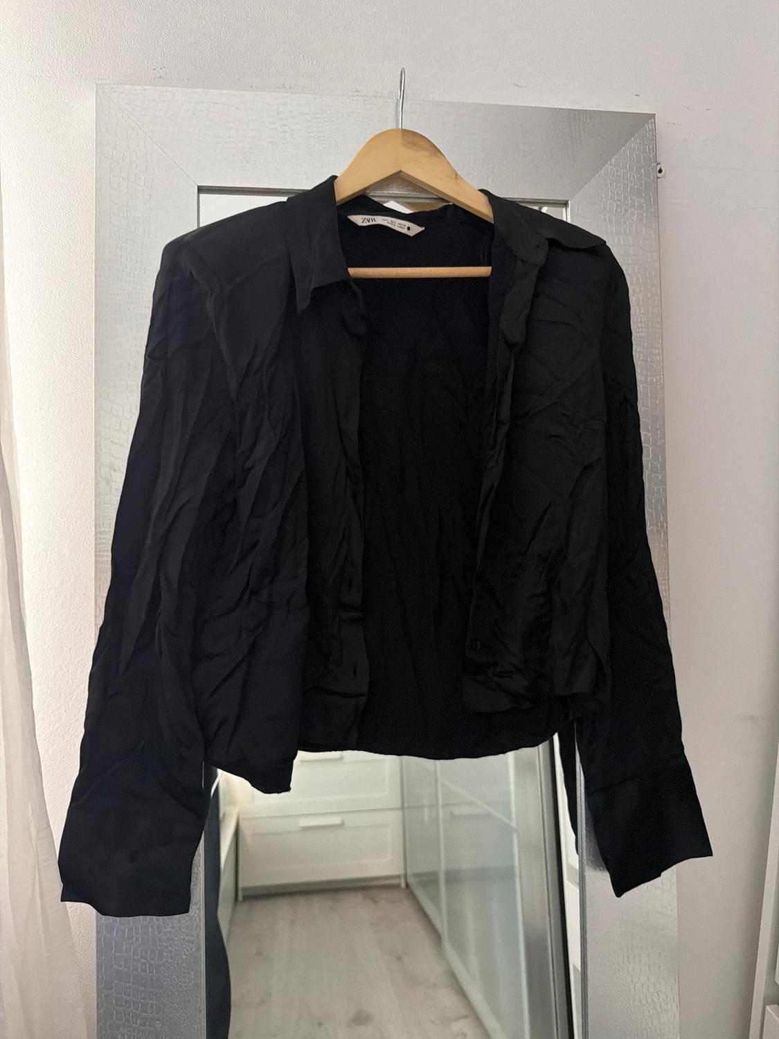 Wrinkled black shirt hanging on a wooden hanger in front of a mirror. Room background with white furniture.