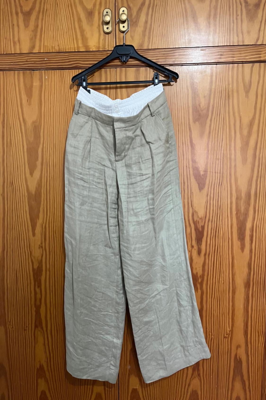 Front view of beige trousers with pleats and side pockets.