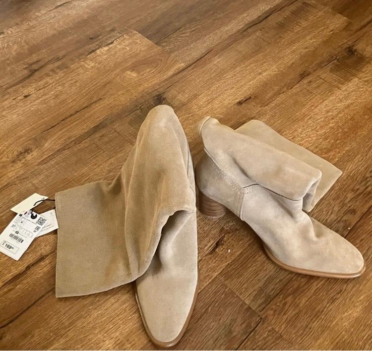 Beige suede boots with wooden heels on a wooden floor. Visible tags with a price of 1,699.