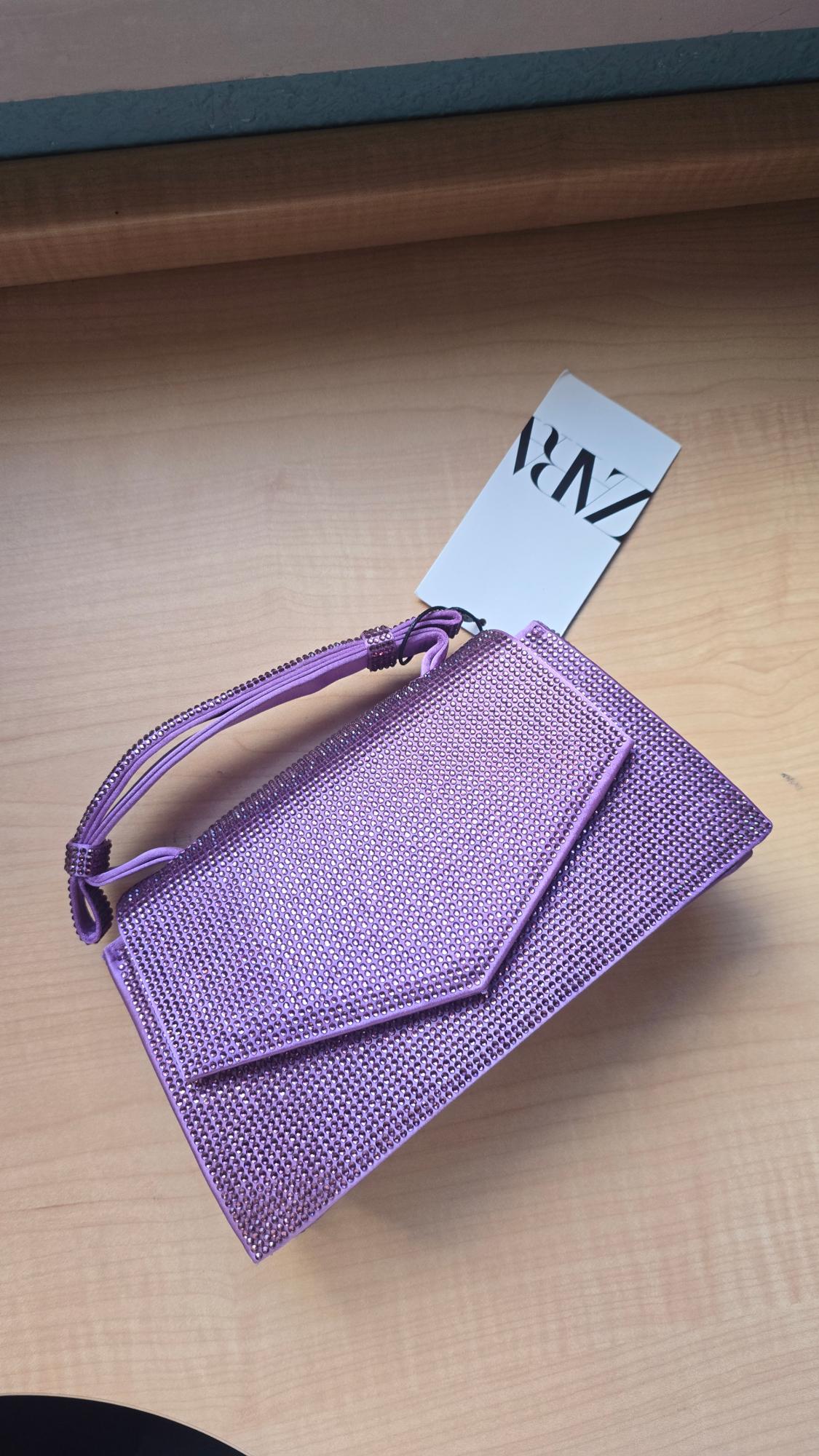 Shiny lilac handbag on a light wooden surface, with a white label that says "ZARA".